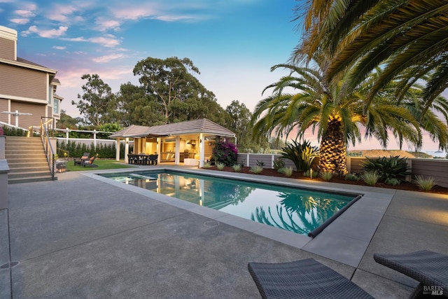 pool at dusk with a fenced in pool, a patio, a fenced backyard, stairs, and an outdoor structure