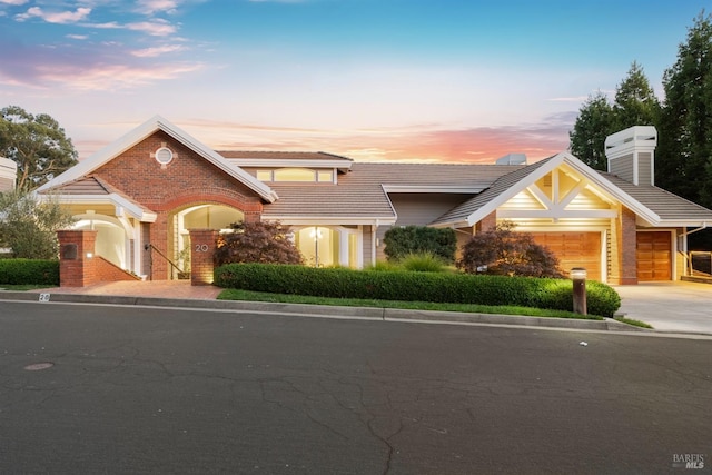 view of front of house featuring a garage, a tiled roof, concrete driveway, and brick siding