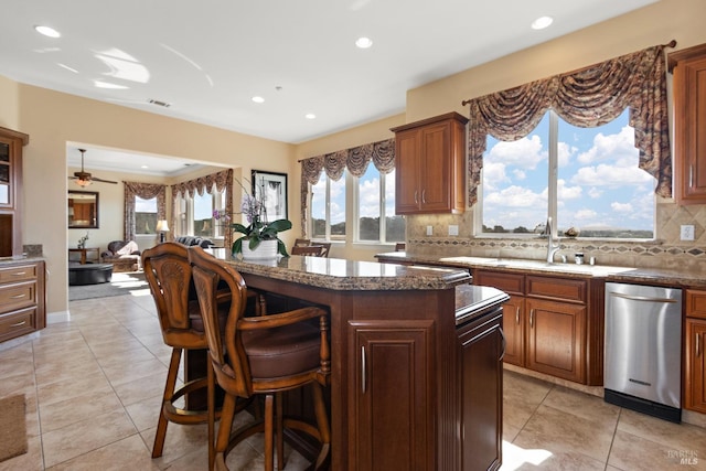 kitchen with a breakfast bar, backsplash, a center island, stainless steel dishwasher, and light tile patterned floors