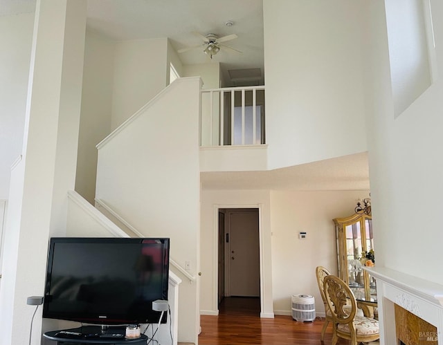 living area with stairway, a ceiling fan, wood finished floors, and a towering ceiling