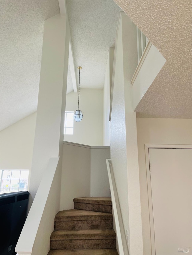stairway with a textured ceiling and lofted ceiling