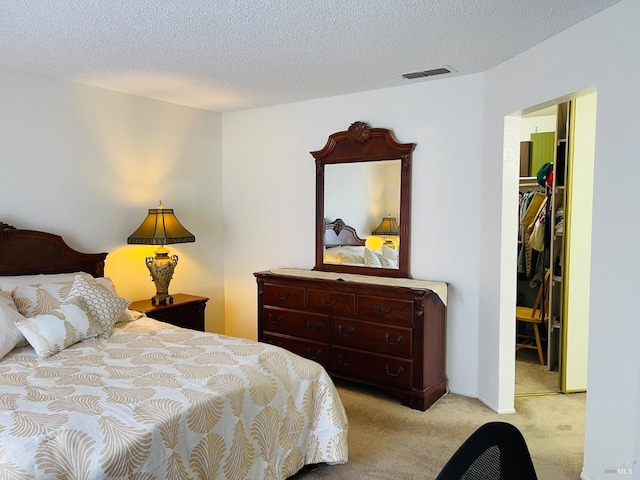 bedroom featuring a textured ceiling, visible vents, light carpet, and a walk in closet