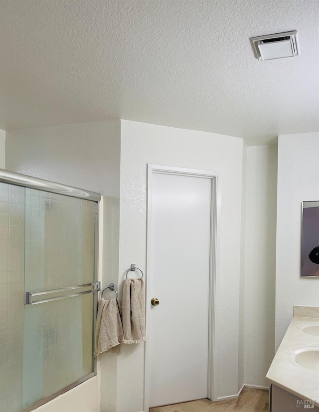 bathroom featuring double vanity, a textured ceiling, visible vents, and shower / bath combination with glass door
