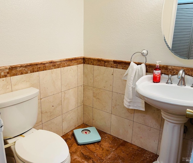 bathroom featuring toilet, tile walls, and wainscoting