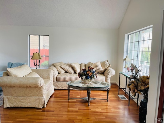 living area with visible vents, a textured ceiling, wood finished floors, and vaulted ceiling