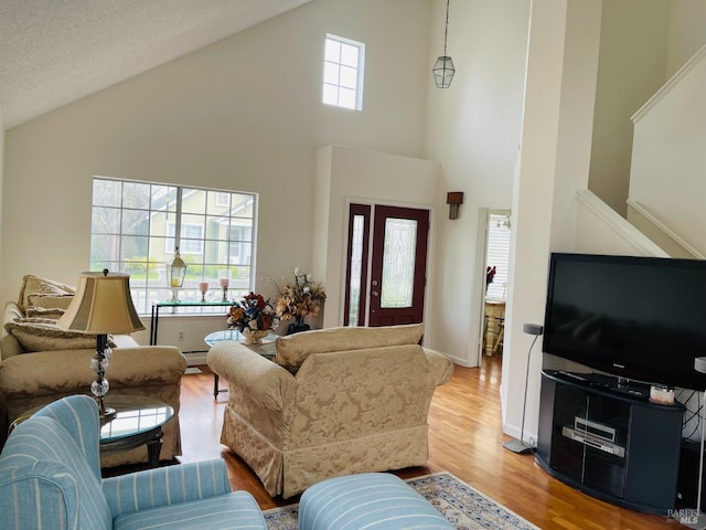 living area featuring high vaulted ceiling, baseboard heating, stairs, and light wood-style flooring