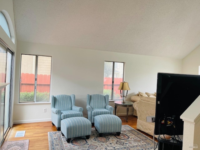 sitting room featuring a textured ceiling, visible vents, light wood-style flooring, and lofted ceiling