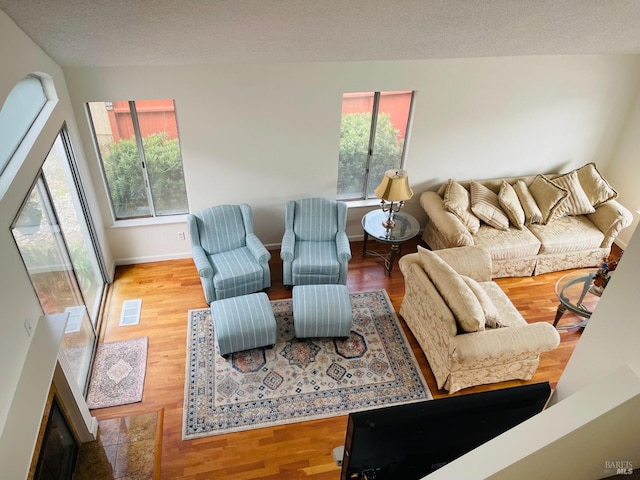living area with baseboards, a textured ceiling, wood finished floors, and visible vents