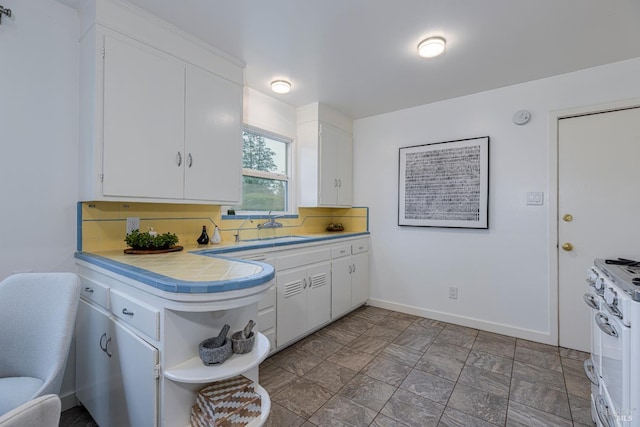 kitchen featuring white cabinetry, tile countertops, gas range gas stove, sink, and backsplash