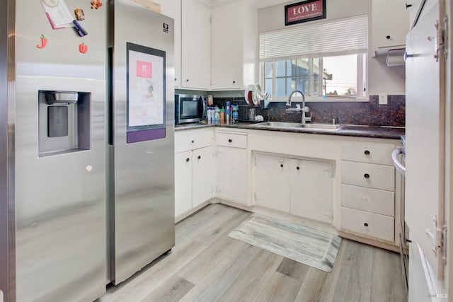 kitchen with white cabinets, light wood finished floors, stainless steel appliances, backsplash, and a sink