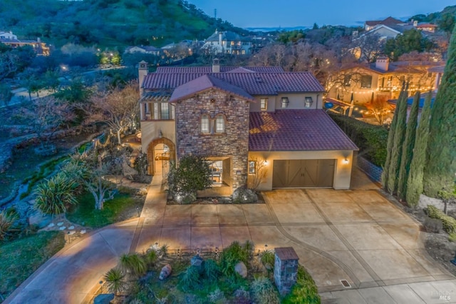 mediterranean / spanish-style house featuring stucco siding, a garage, stone siding, driveway, and a tiled roof