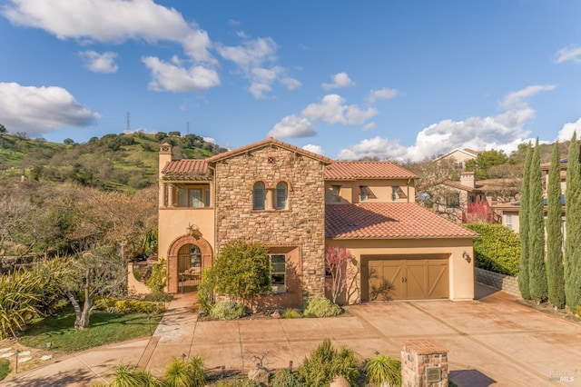 mediterranean / spanish house featuring a garage, a tile roof, concrete driveway, stone siding, and stucco siding