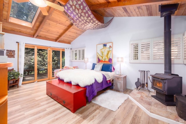 bedroom featuring a wood stove, access to exterior, light wood-type flooring, and beam ceiling