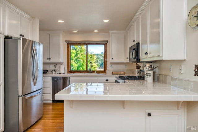 kitchen with tile countertops, white cabinets, stainless steel appliances, and kitchen peninsula