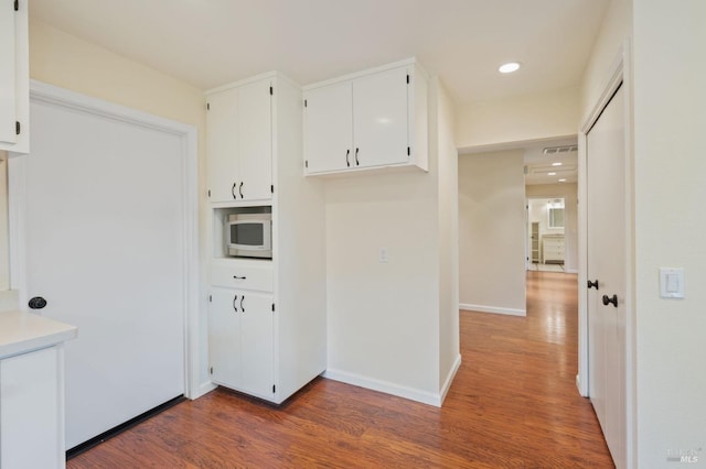 kitchen featuring baseboards, white cabinets, stainless steel microwave, dark wood-style flooring, and recessed lighting