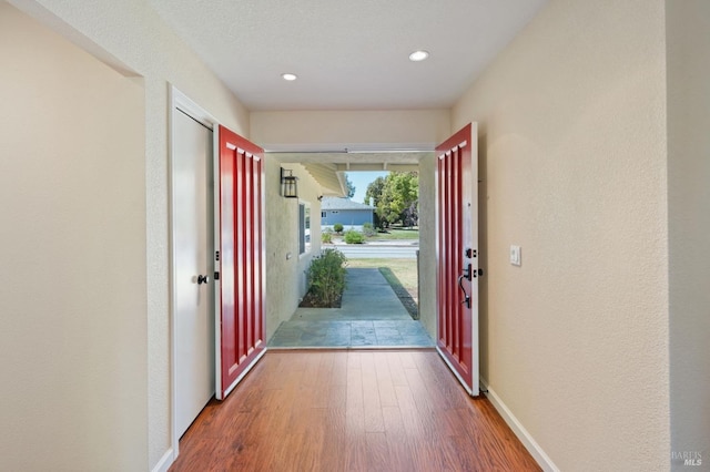 doorway with recessed lighting, a textured wall, baseboards, and wood finished floors