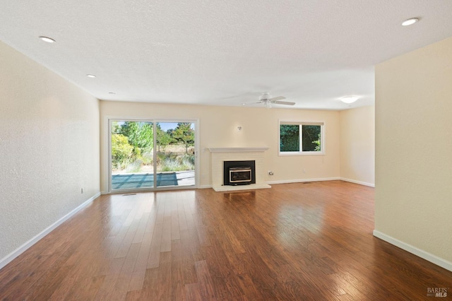 unfurnished living room featuring dark wood finished floors, a textured wall, a glass covered fireplace, a textured ceiling, and baseboards