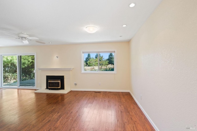 unfurnished living room with a brick fireplace, baseboards, a wealth of natural light, and wood finished floors