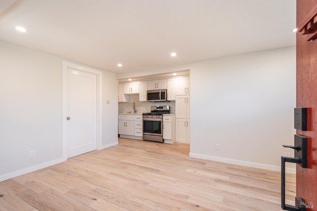 1008 Evans Ave, Napa, CA 94559 - kitchen featuring backsplash, appliances with stainless steel finishes, light wood-type flooring, baseboards, and white cabinets