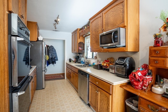 kitchen with appliances with stainless steel finishes, light countertops, a sink, and light floors