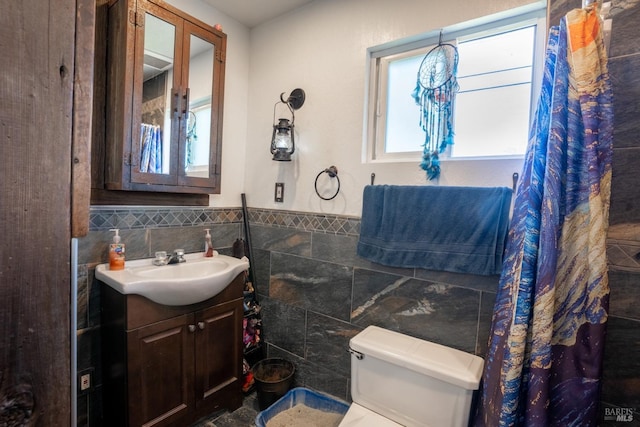 bathroom with toilet, a wainscoted wall, vanity, and tile walls