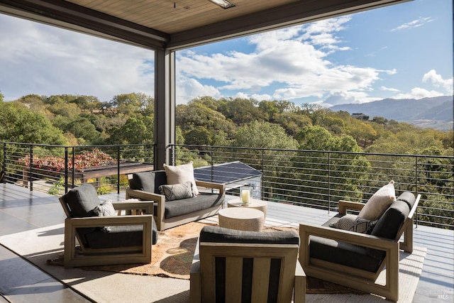 view of patio featuring an outdoor living space, a mountain view, a view of trees, and a balcony