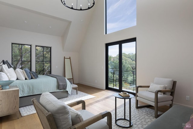 bedroom with access to exterior, a towering ceiling, a chandelier, light wood-type flooring, and baseboards