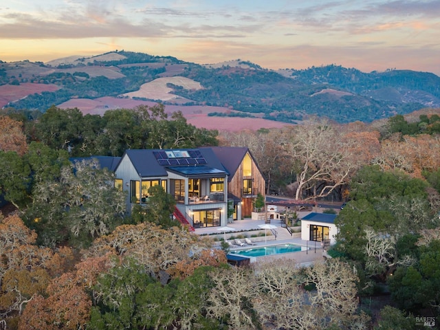 back of property at dusk featuring an outdoor pool, a patio, stairs, roof mounted solar panels, and a mountain view