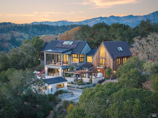 back of house with a mountain view, stairway, roof mounted solar panels, a forest view, and a patio area