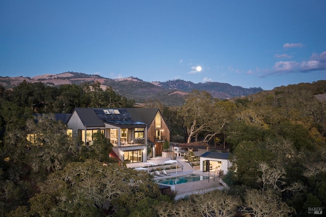 rear view of house with an outdoor pool, an outdoor structure, a patio area, roof mounted solar panels, and a mountain view