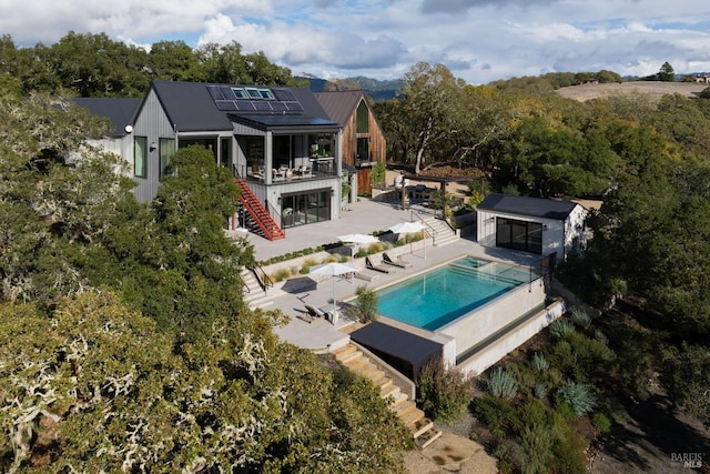 back of house with an outbuilding, a patio, solar panels, an outdoor pool, and stairs