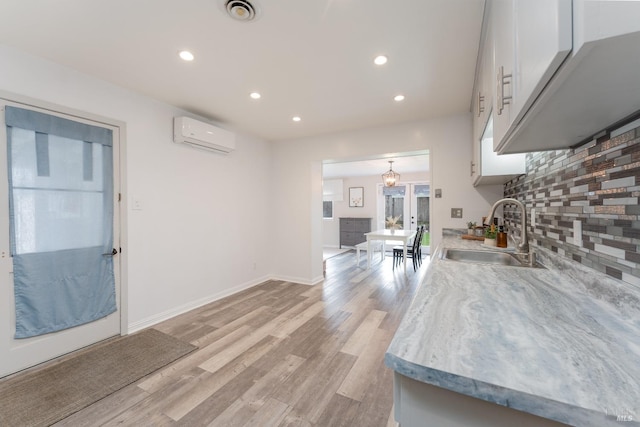 kitchen with visible vents, decorative backsplash, an AC wall unit, white cabinets, and a sink