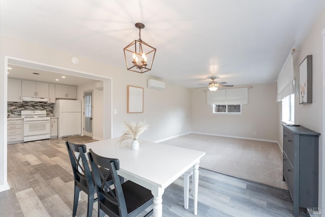 dining space featuring baseboards, ceiling fan with notable chandelier, a wall unit AC, and light wood-style floors