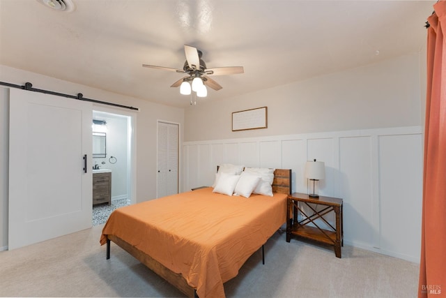 bedroom featuring ensuite bath, a barn door, a decorative wall, and light colored carpet