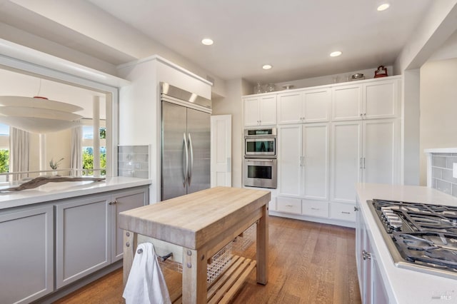 kitchen featuring white cabinets, wood finished floors, stainless steel appliances, light countertops, and backsplash