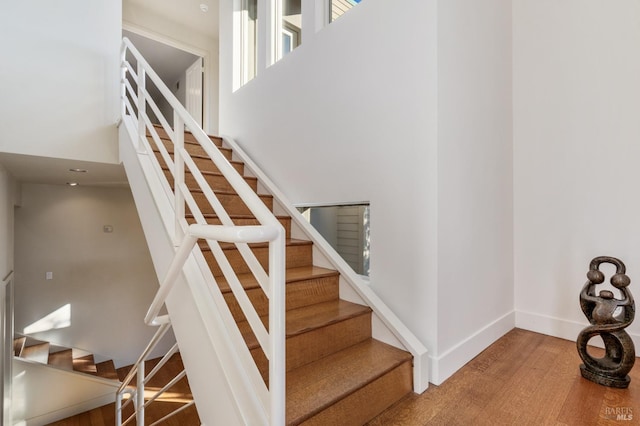 stairs featuring a towering ceiling, baseboards, and wood finished floors