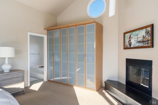 bedroom with connected bathroom, carpet floors, vaulted ceiling, access to outside, and a glass covered fireplace