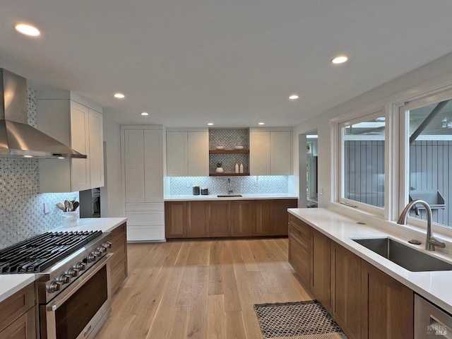 kitchen featuring appliances with stainless steel finishes, wall chimney range hood, light hardwood / wood-style floors, sink, and white cabinetry