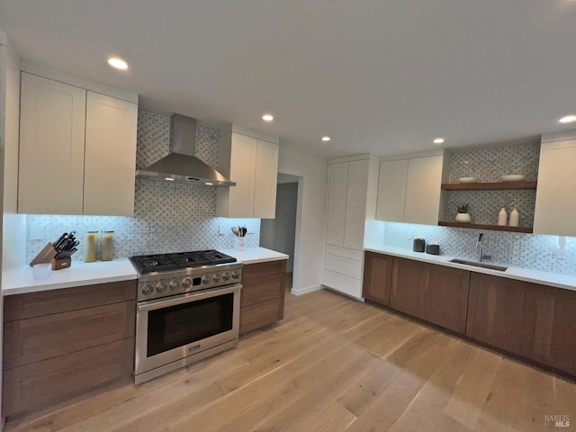 kitchen with light hardwood / wood-style floors, sink, stainless steel gas range oven, white cabinets, and wall chimney range hood