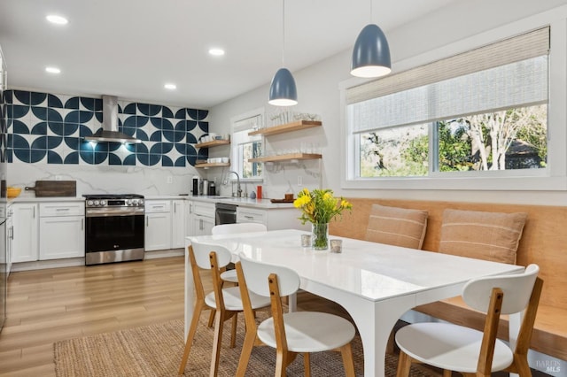 kitchen featuring stainless steel range with gas cooktop, white cabinetry, sink, wall chimney range hood, and pendant lighting