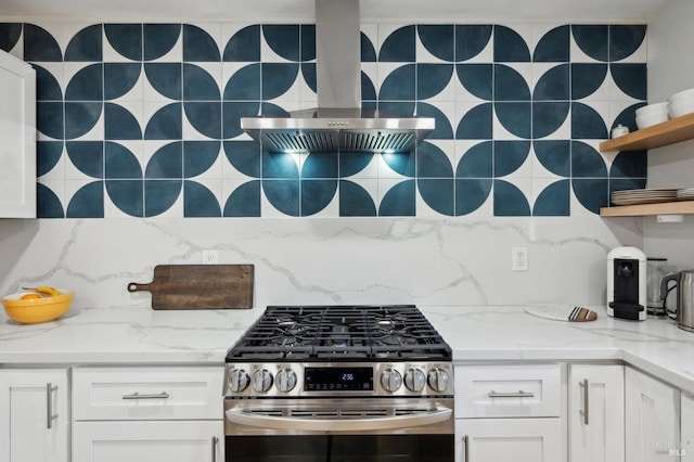 kitchen with stainless steel gas stove, light stone counters, white cabinetry, and backsplash