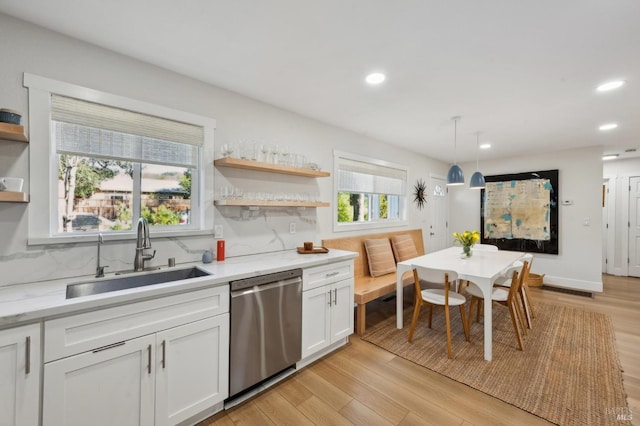 kitchen with sink, light stone counters, white cabinetry, pendant lighting, and stainless steel dishwasher