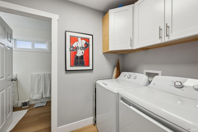 clothes washing area with cabinets, light wood-type flooring, and washing machine and clothes dryer