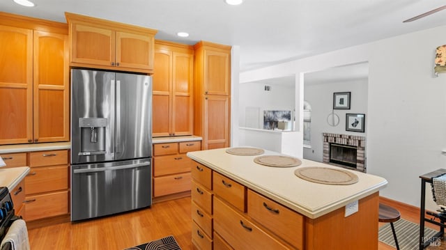 kitchen featuring light wood-style flooring, a kitchen island, light countertops, a brick fireplace, and stainless steel fridge with ice dispenser