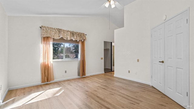 unfurnished bedroom with light wood-style floors, ceiling fan, baseboards, and high vaulted ceiling