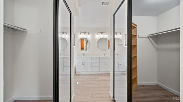 walk in closet with light wood-style flooring, a sink, and visible vents