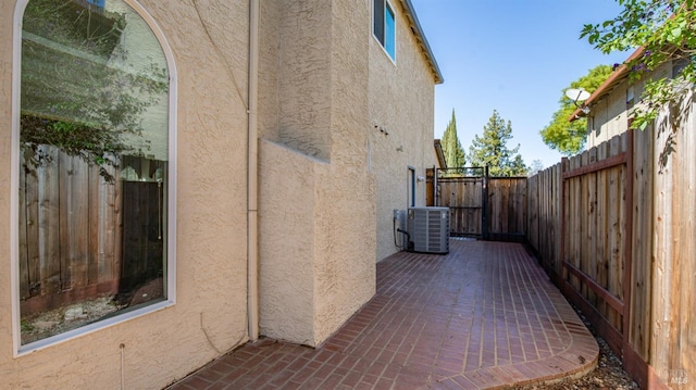 view of side of property featuring a patio area, fence, central AC, and stucco siding