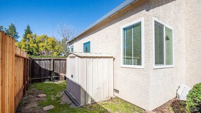 view of side of property featuring stucco siding, a storage shed, crawl space, a fenced backyard, and an outdoor structure