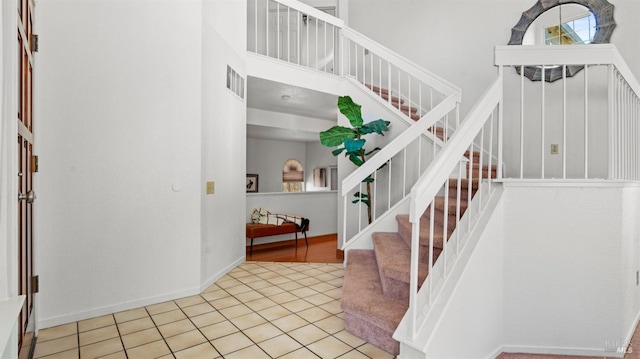 staircase featuring a towering ceiling, tile patterned flooring, visible vents, and baseboards