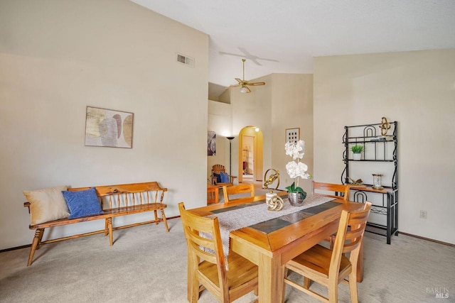 carpeted dining area featuring baseboards, visible vents, arched walkways, a ceiling fan, and high vaulted ceiling